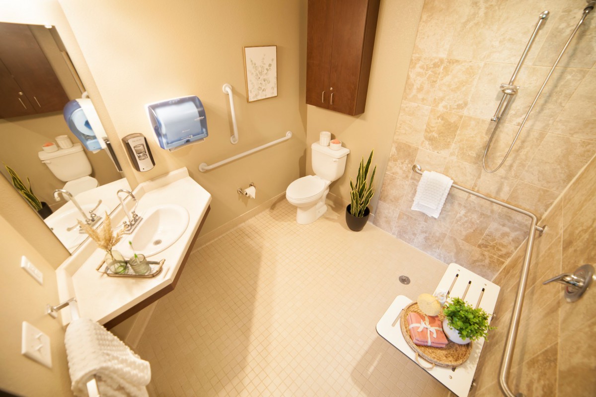 A modern bathroom featuring a sink, toilet, towel rack, and shower chair with beige walls and an indoor plant for decoration.