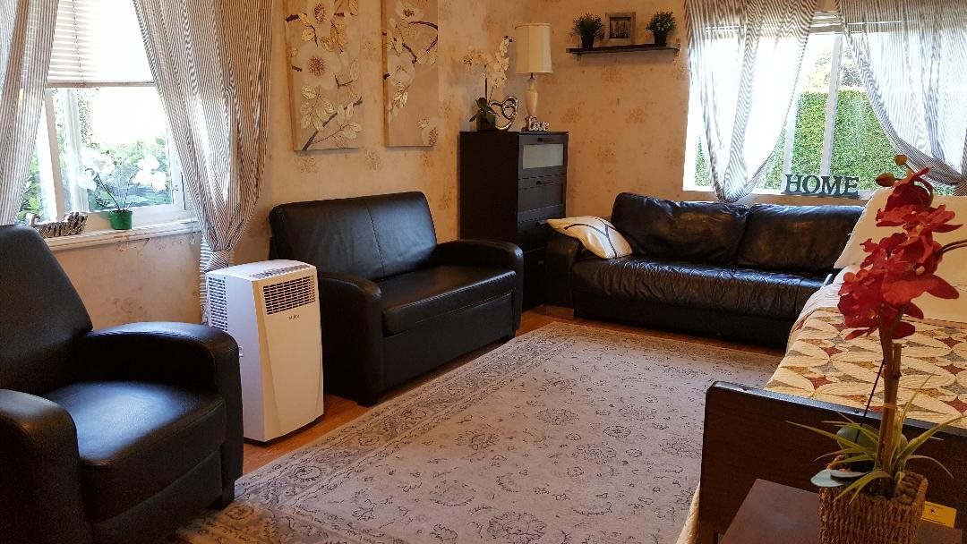 A cozy living room with dark leather sofas, a carpet, and an air conditioner.