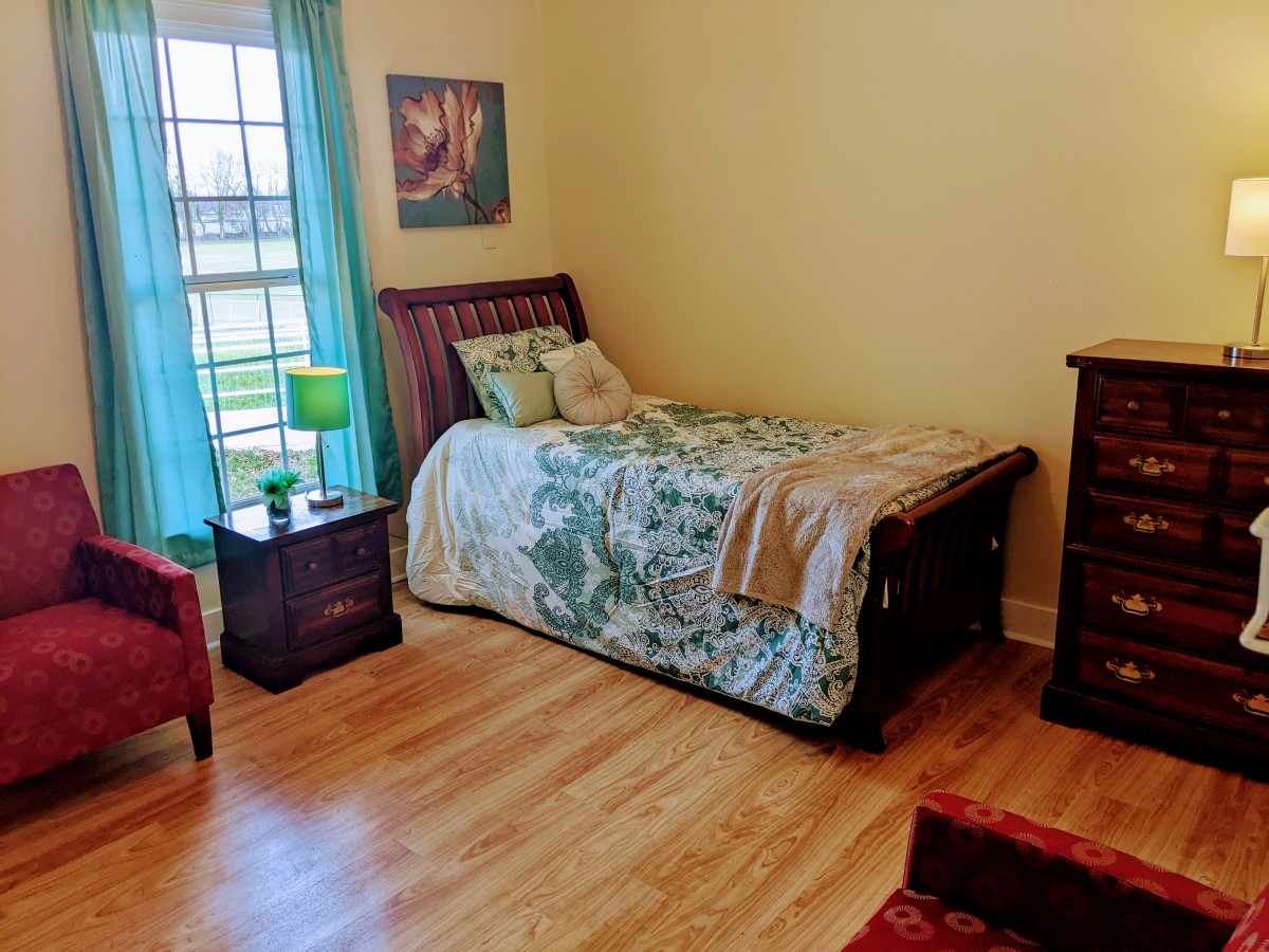A cozy bedroom with a single bed, nightstand, and hardwood flooring.