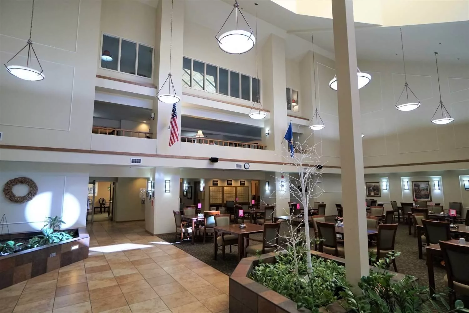 A spacious lobby with an atrium, featuring seating areas, flags, and indoor plants.