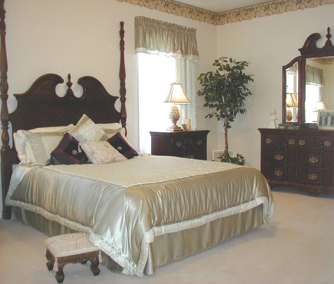 A traditional bedroom featuring a bed with a headboard, matching dresser and nightstand, a lamp, and decorative elements including a potted plant.