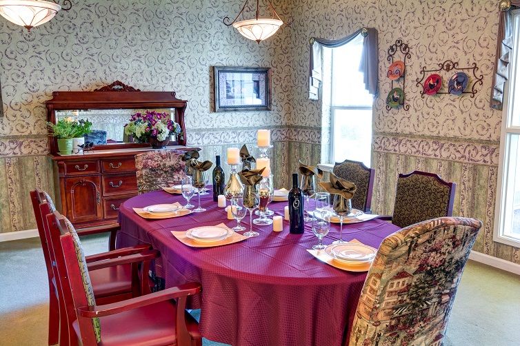A beautifully set dining table with a burgundy tablecloth, complete with wine bottles and candles, in an elegantly decorated dining room.
