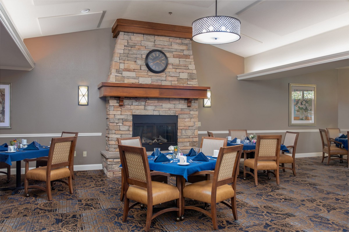 A cozy dining area featuring a stone fireplace and elegantly set tables with blue tablecloths.