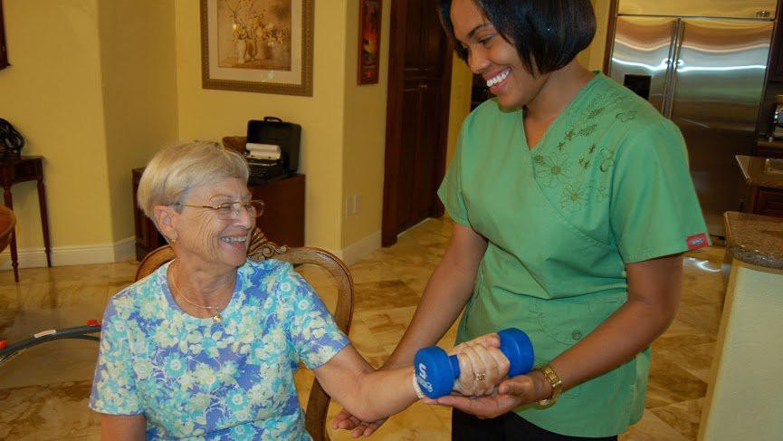 A healthcare worker assists a senior woman with physical therapy exercises.