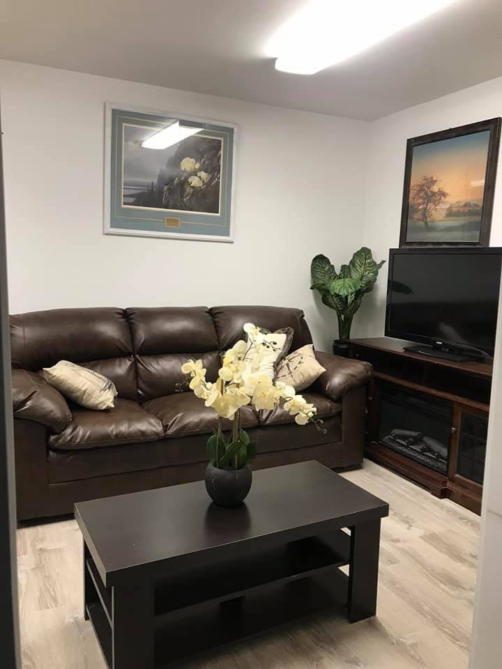 A cozy living room with a leather sofa, television, decorative plants, and framed art on the walls.