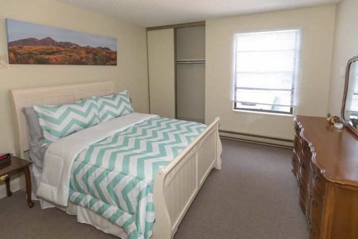 A cozy bedroom with a neatly made bed featuring a zigzag patterned duvet, a window allowing natural light, and an open closet.