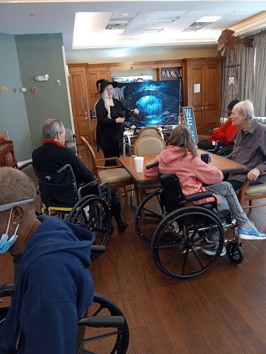 A group of elderly individuals in wheelchairs participating in a community activity, with a presenter sharing information in a warm, inviting setting.