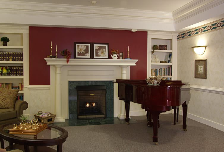 A cozy living room featuring a fireplace and a grand piano against a red accent wall.