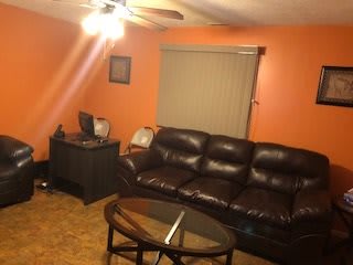 A cozy living room with an orange accent wall, featuring a leather sofa and a glass coffee table.