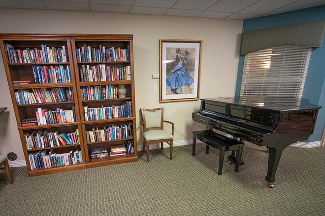 A cozy library corner with a bookshelf, piano, and chair.