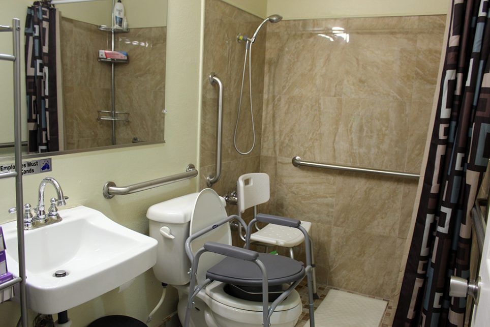 An accessible bathroom equipped with grab bars, a shower chair, and toilet aids.