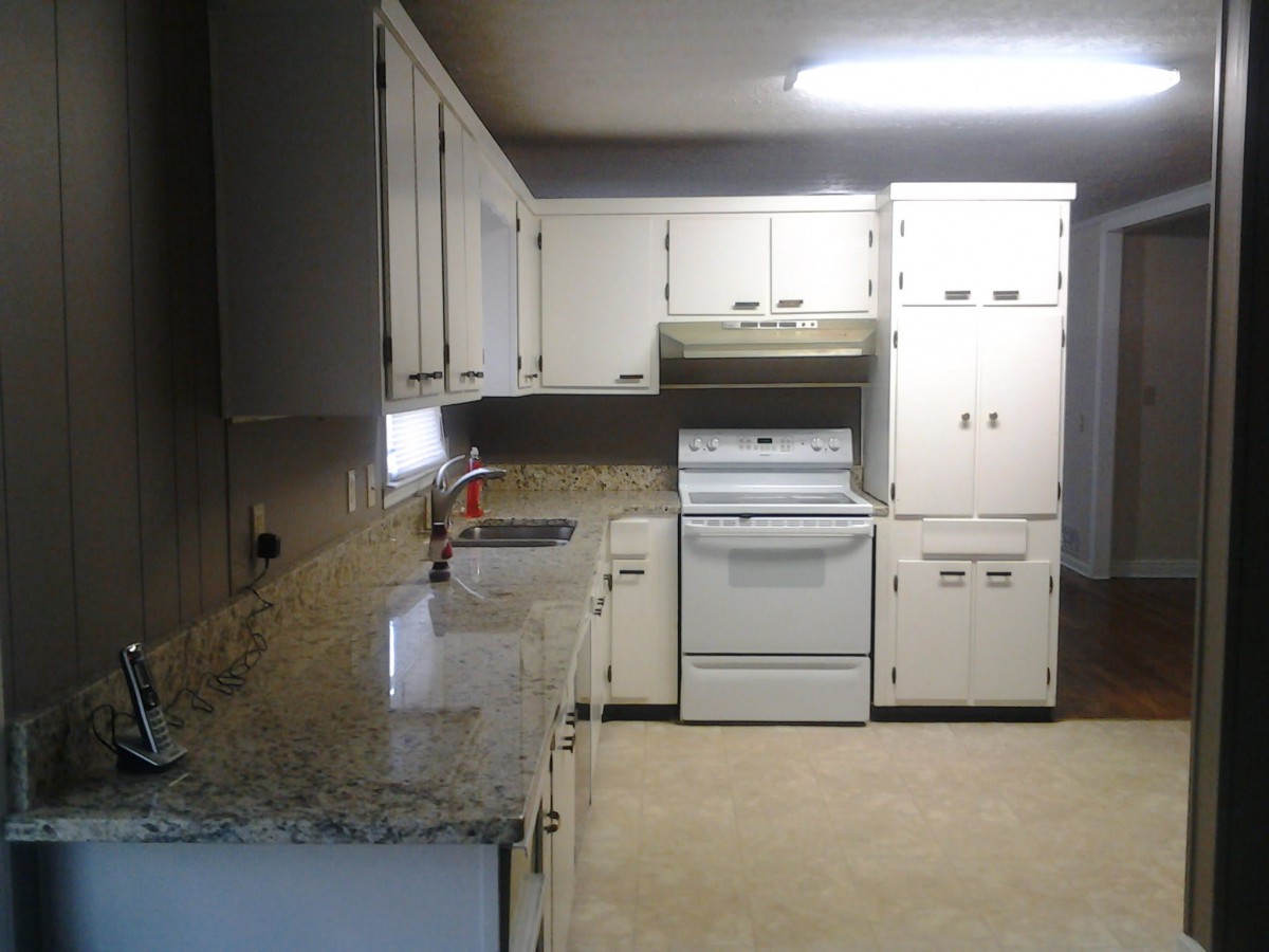 A kitchen with white cabinets and appliances, featuring a marble countertop.