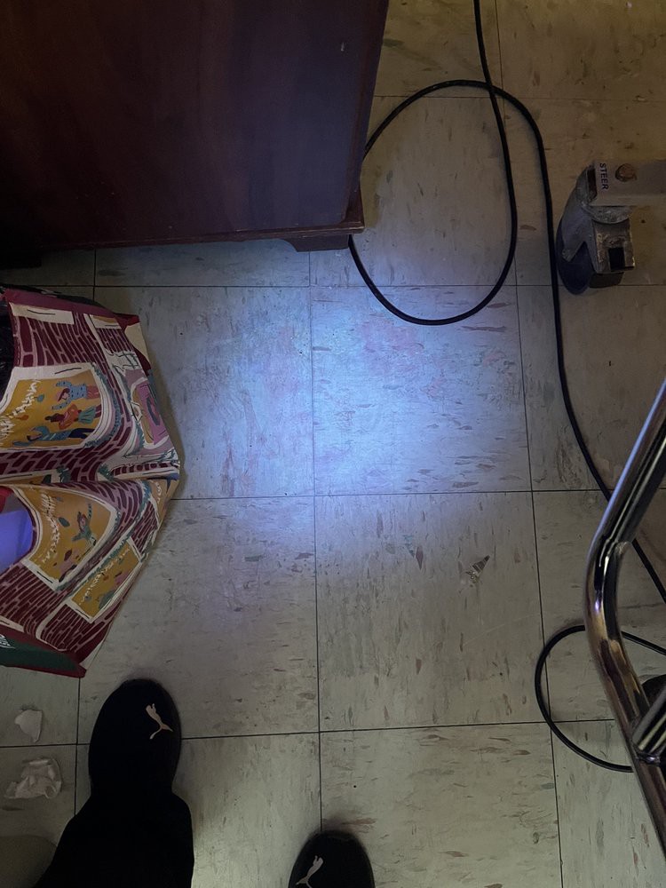 A tiled floor with a light shining, revealing a pattern and some cords nearby.