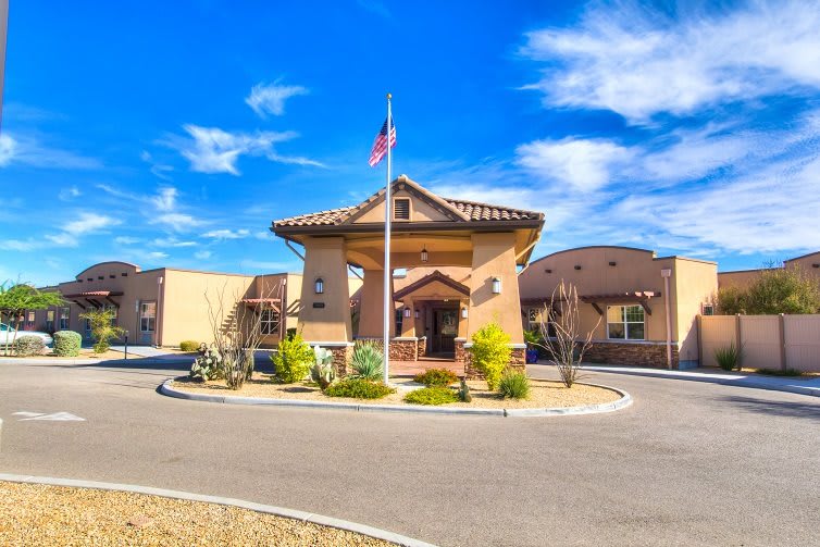 A sunny day view of a building with an entrance, landscaping, and an American flag.