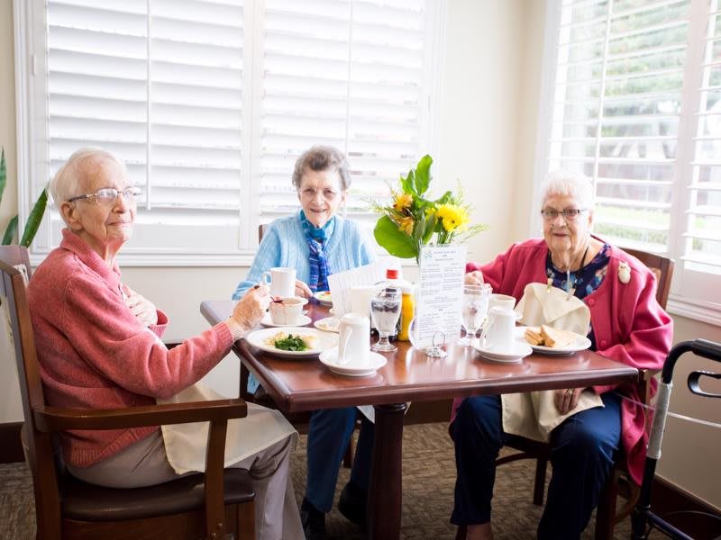 Three seniors enjoying a meal together at a dining table.