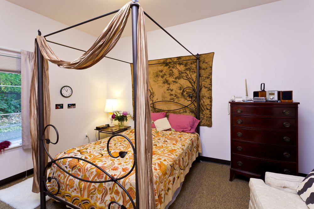 A cozy bedroom featuring a canopy bed with ornate metalwork, complemented by a tapestry and warm lighting.