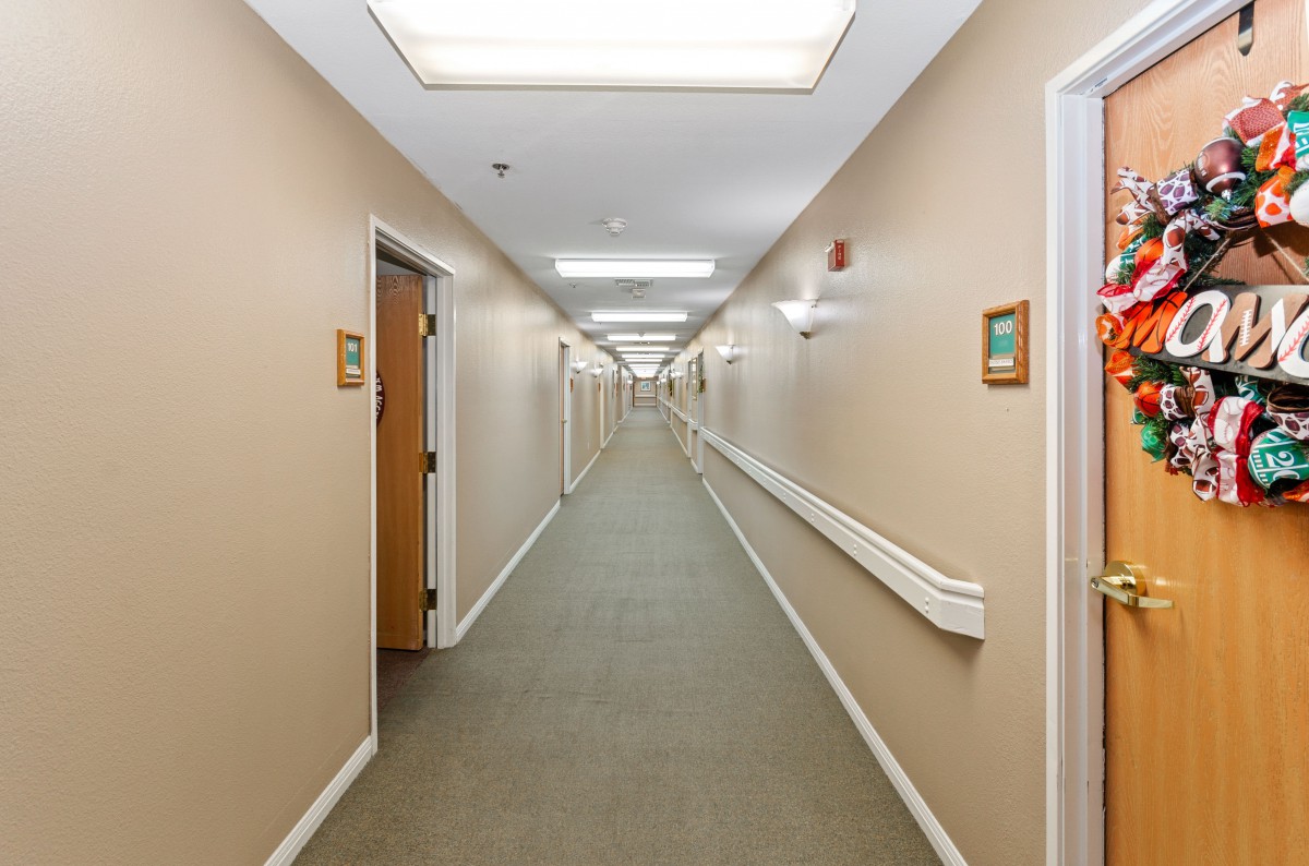 A long, well-lit hallway with beige walls and multiple doors on either side.