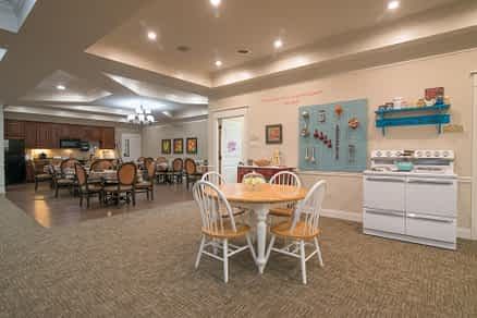 A cozy dining and kitchen area with ambient lighting, featuring a central table and chairs surrounded by decorative elements.