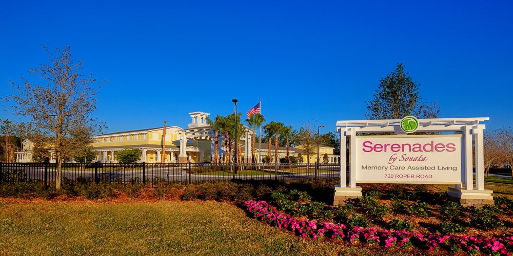 A well-maintained building surrounded by palm trees and vibrant flowers under a clear blue sky.