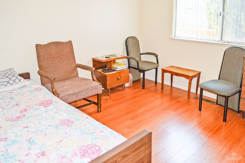 A simple bedroom with chairs, a side table, and a window.