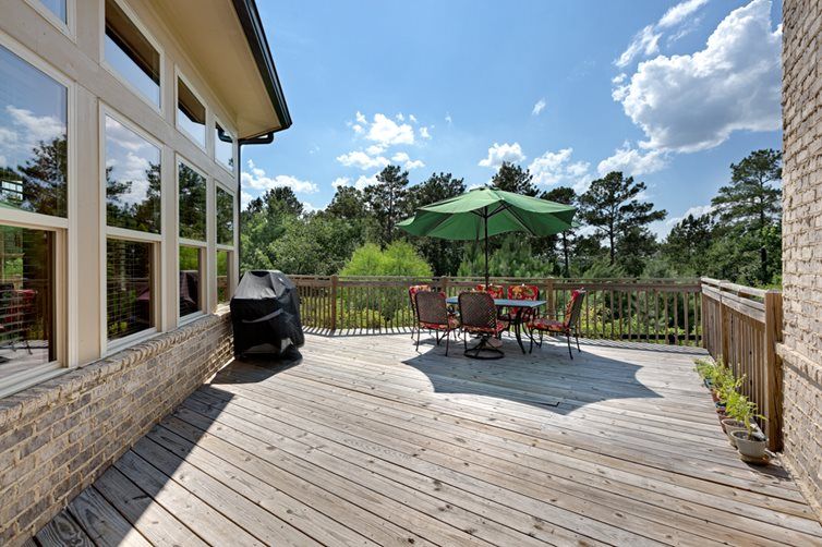 A spacious wooden deck with a table, chairs, and an umbrella, surrounded by nature on a sunny day.