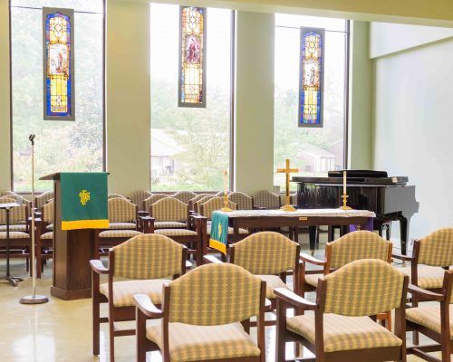 A serene chapel interior featuring an altar, seating, and stained glass windows.