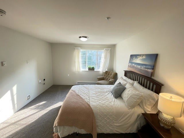 A minimalist bedroom with a bed, chair, and window letting in natural light.