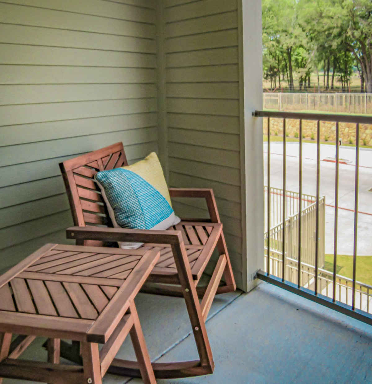 A cozy balcony setup with wooden chairs and a table, complemented by colorful cushions.