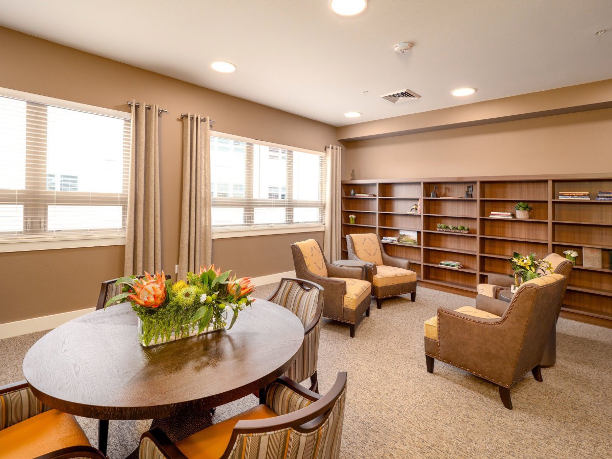 A cozy, well-lit living room with comfortable chairs, a round table, and bookshelves.