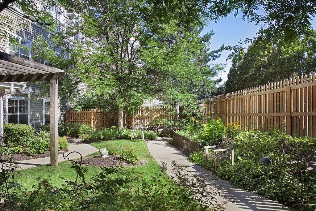 A serene garden with lush greenery, featuring a winding pathway and wooden fence.