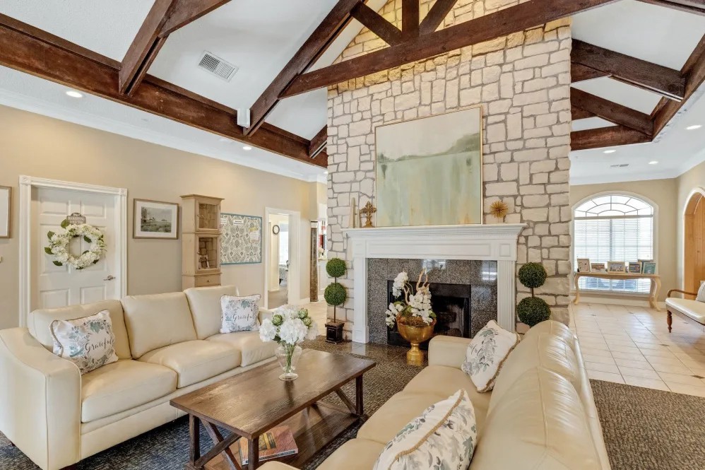 A cozy living room featuring a stone fireplace and wooden beam ceiling.