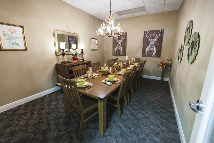 A well-appointed dining room with a long wooden table set for dinner, surrounded by chairs and illuminated by a chandelier.