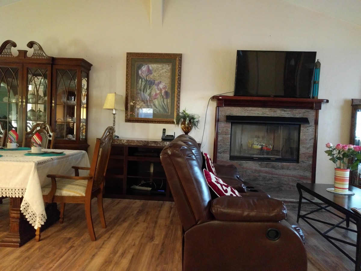 A cozy living room featuring a leather chair, a fireplace, and a television, adjacent to a dining area with elegant furniture and artwork on the wall.
