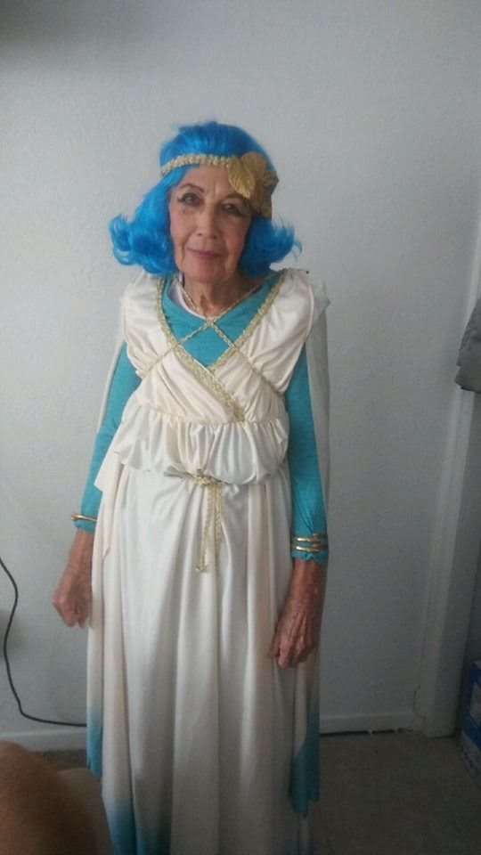 Elderly woman in a blue wig and white costume.