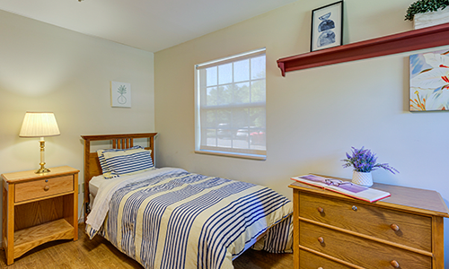 A cozy bedroom featuring a single bed with striped bedding, a small window, and minimalist decor.