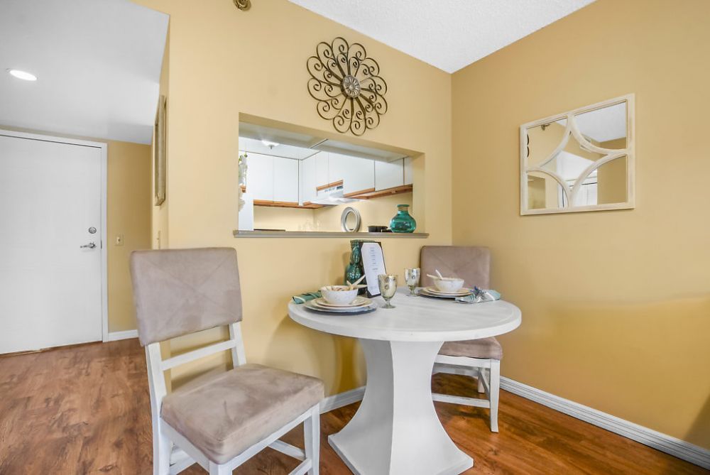 A cozy dining setup with a round table and two chairs, adjacent to a kitchen pass-through window with modern decor.