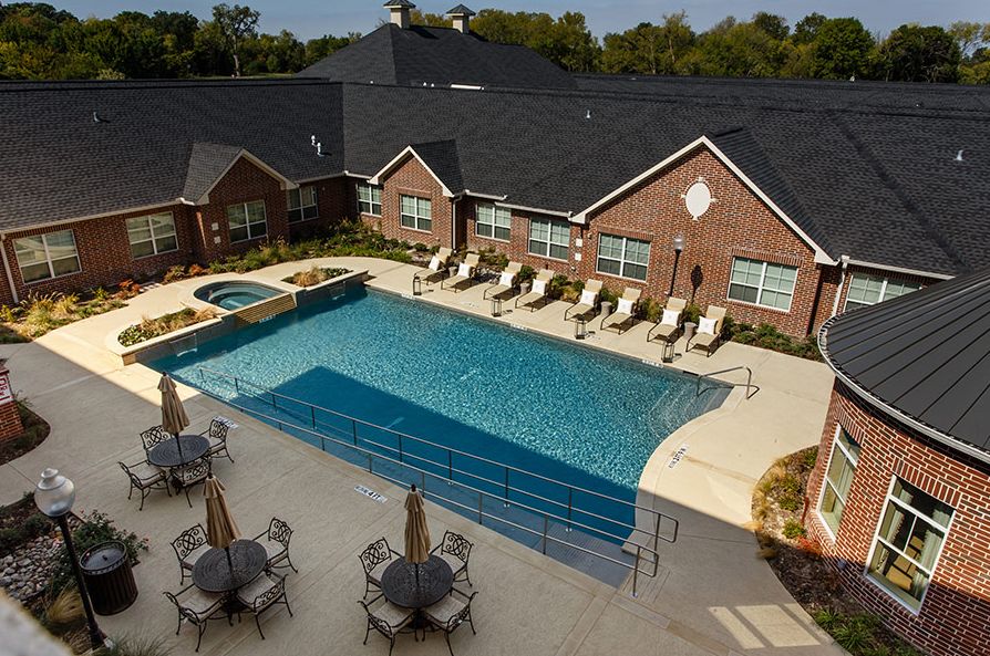 A residential outdoor swimming pool area with sun loungers and patio furniture near a brick building.