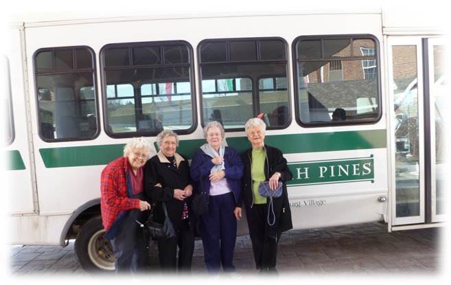 A group of elderly friends posing in front of a bus.