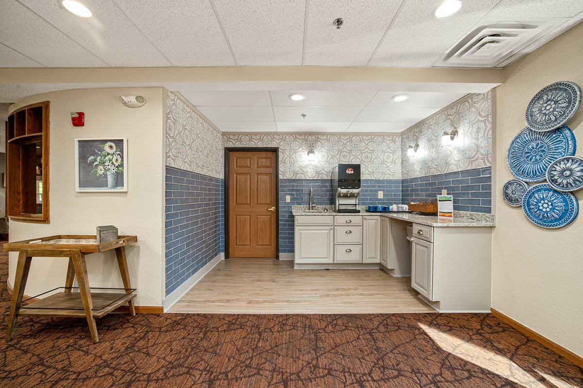 A kitchenette area featuring a coffee station, cabinets, and distinct tile and carpet flooring.