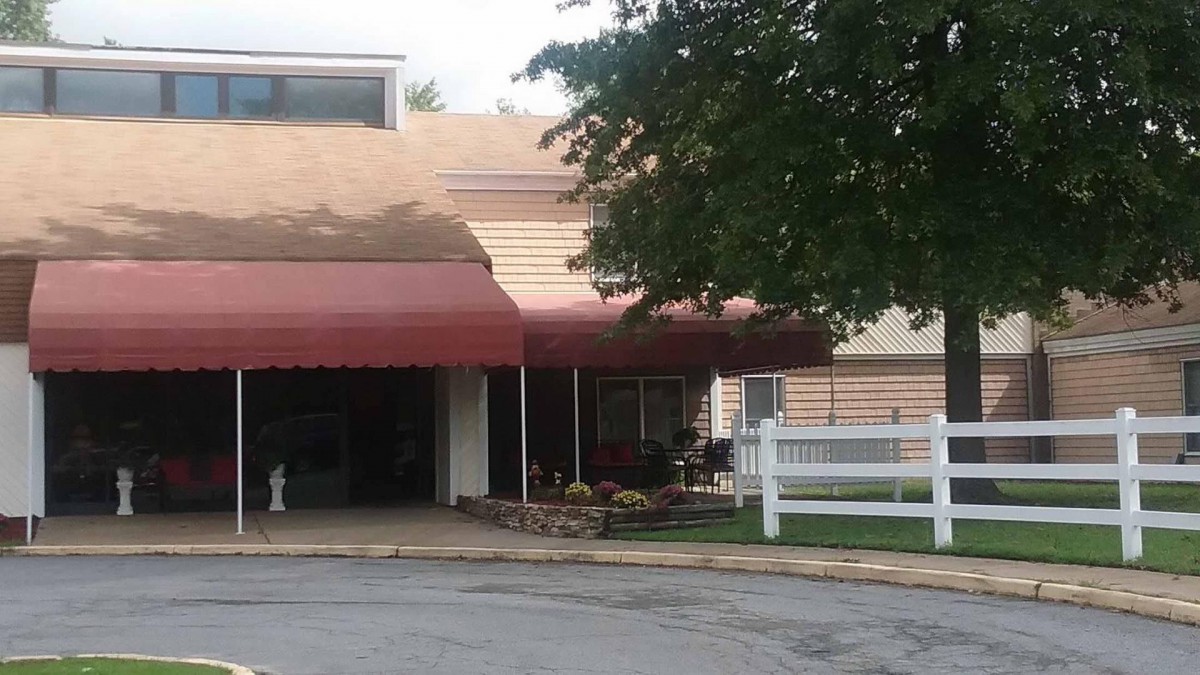 A building entrance with a red awning and a nearby tree and fence.