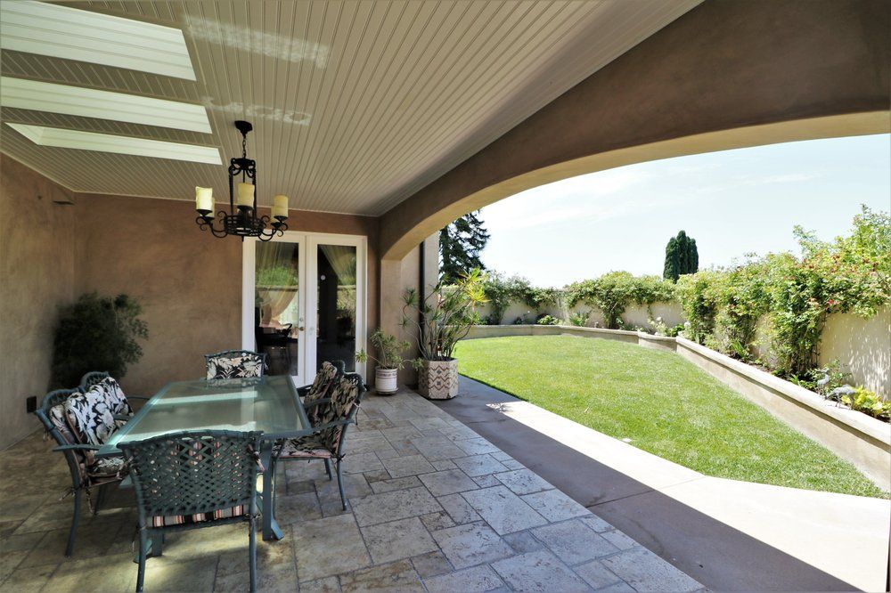 A covered patio with outdoor furniture overlooking a well-maintained lawn and garden.