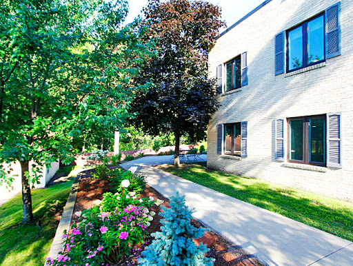 A serene pathway lined with colorful flowers and trees, leading to a modern building.