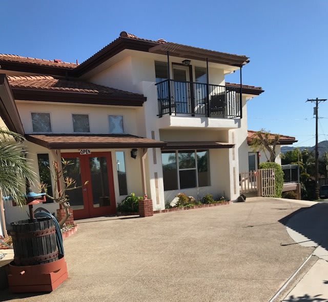 A modern two-story house with a red tile roof and spacious driveway under a clear blue sky.
