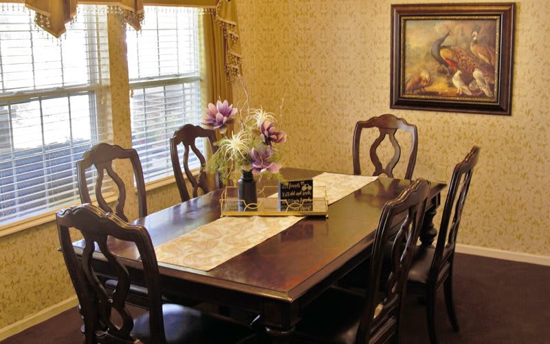 A classic dining room with a wooden table and chairs, featuring a floral centerpiece.