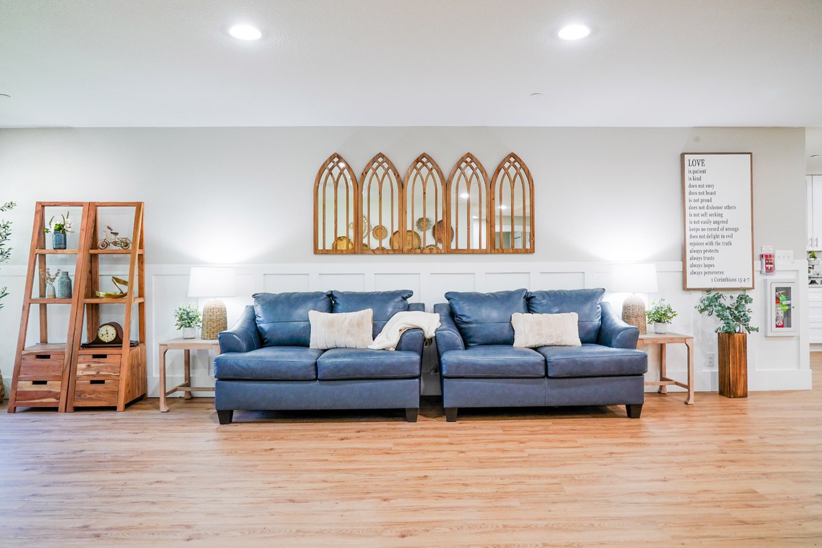 A modern living room featuring two blue sofas, wooden flooring, and decorative mirror art on the wall.