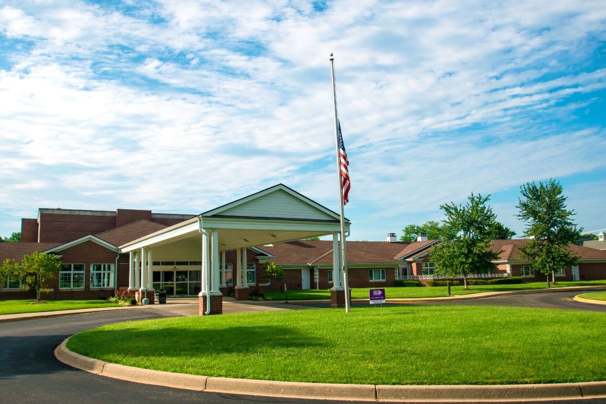 A building with an entrance and a flagpole stands against a partly cloudy sky, surrounded by a well-maintained lawn.