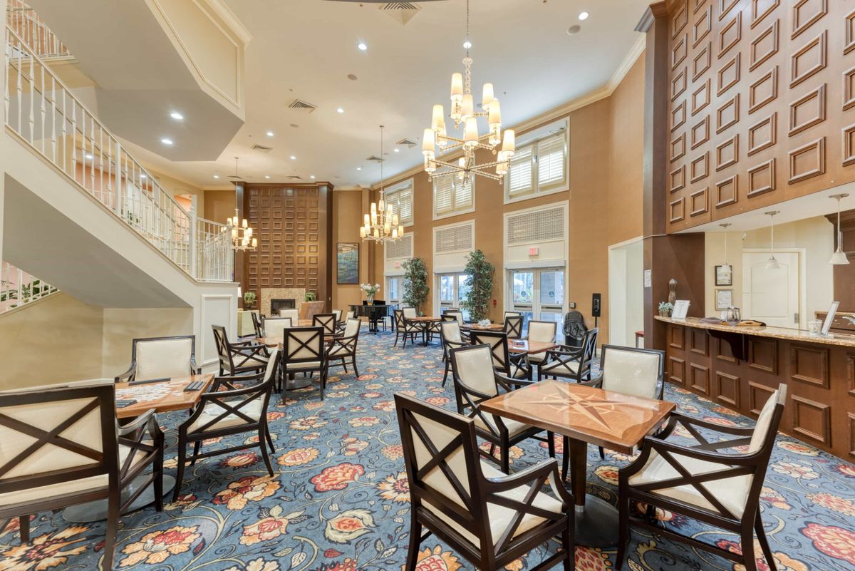 An elegant dining area with chandeliers, tables, and chairs arranged on a patterned carpet.