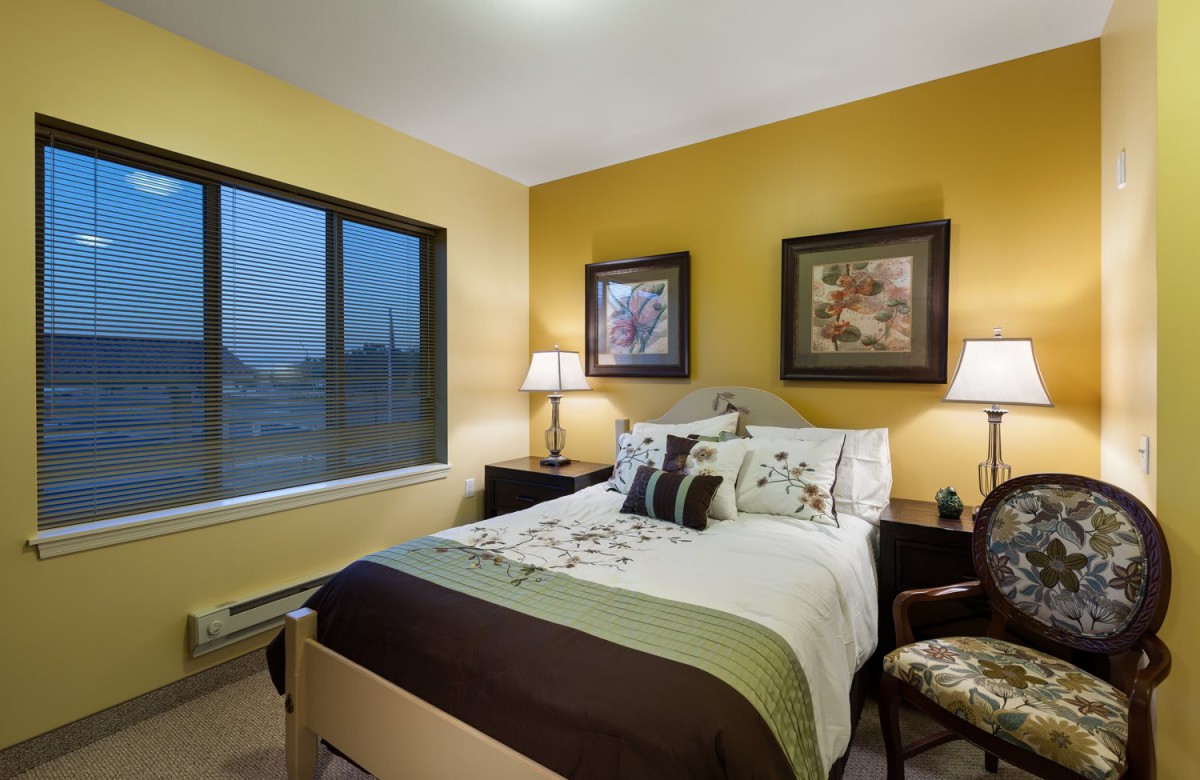 A cozy bedroom with warm yellow walls, featuring a neatly made bed and elegant decor.
