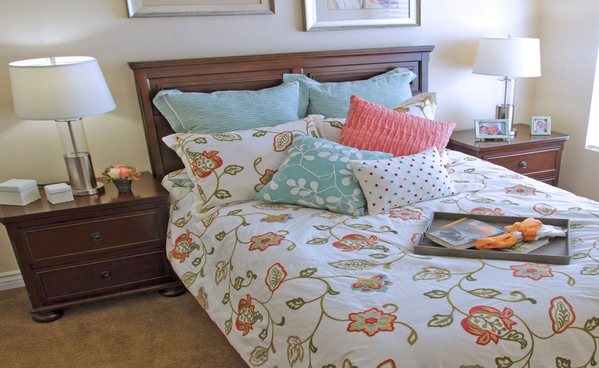 A cozy bedroom setup with floral-patterned bedding and a variety of decorative pillows.