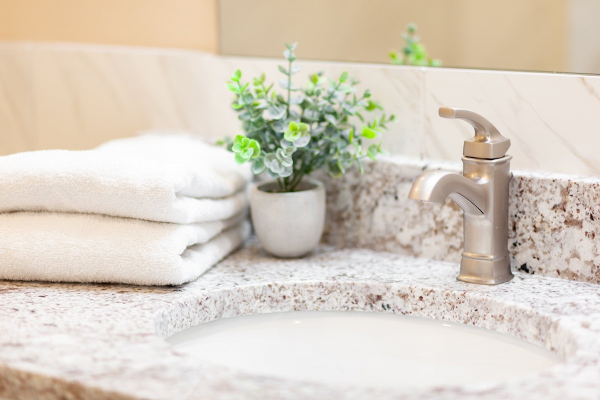 A neatly arranged bathroom countertop featuring a faucet, stacked white towels, and a small potted plant.